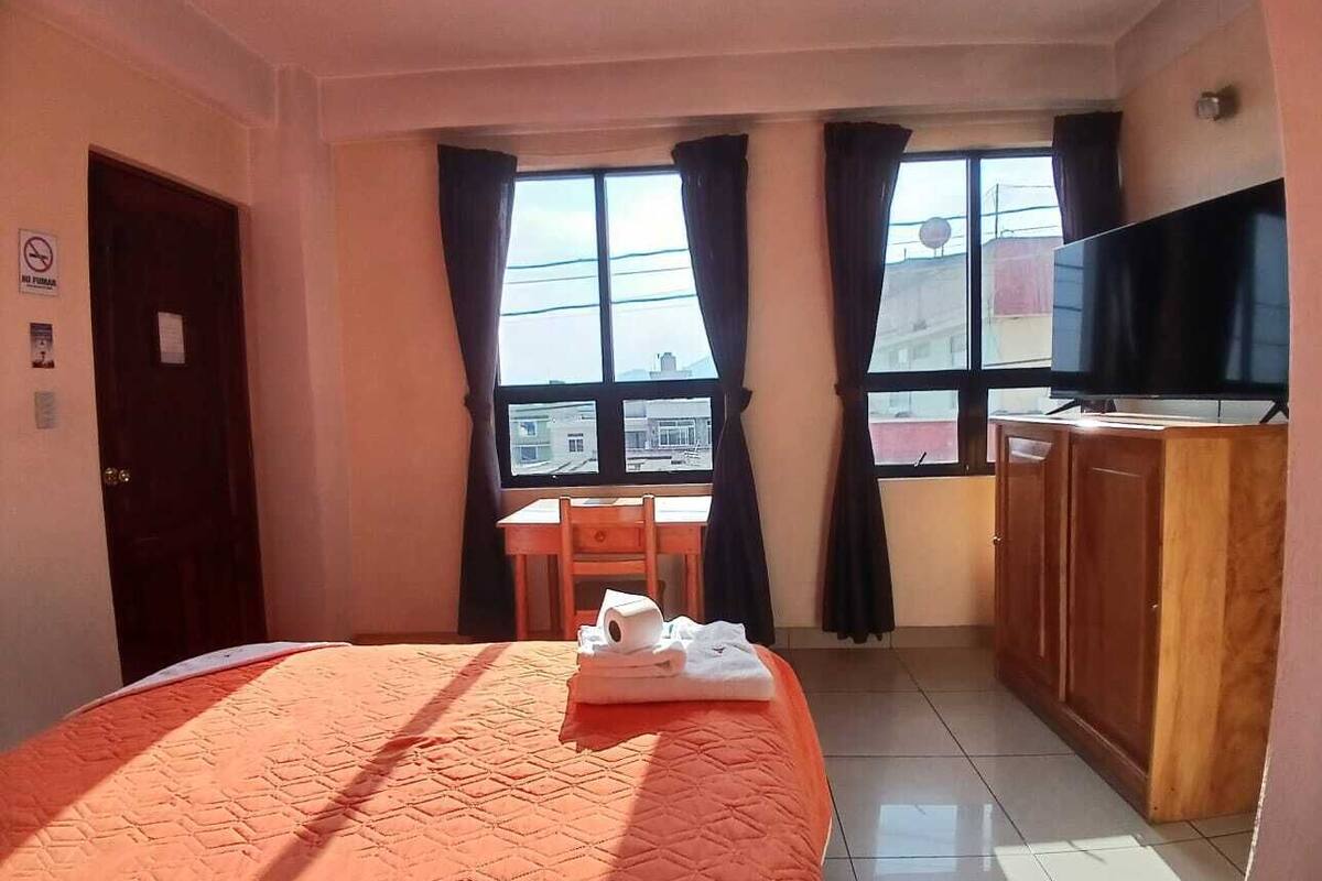A hotel room with a bed, a desk, a chair, a television, and a window with curtains.