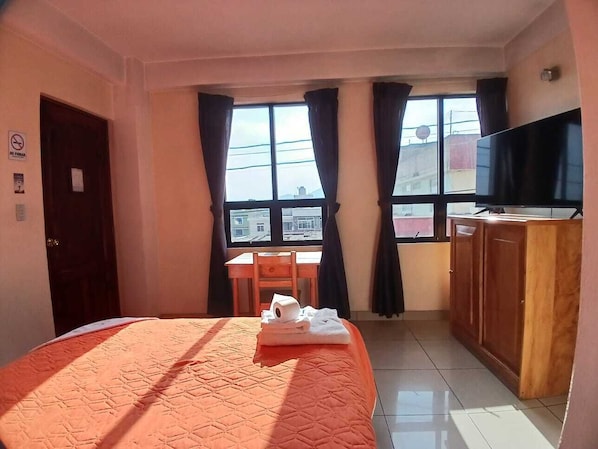 A hotel room with a bed, a desk, a chair, a television, and a window with curtains.