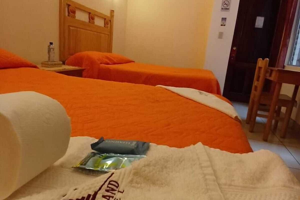 A hotel room with two beds, a wooden headboard, a nightstand, a chair, and a wall-mounted light.