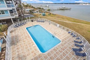 A swimming pool with a tiled deck, lounge chairs, and a view of a body of water and buildings. - Lagoon Front Living Steps to Beach + Dock + Pool (Gulf Shores)