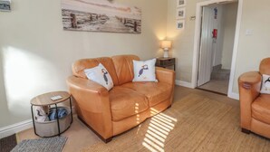 A living room with a brown leather sofa, a rug, a lamp, and a painting on the wall. - Puffin's Nest (Bridlington)