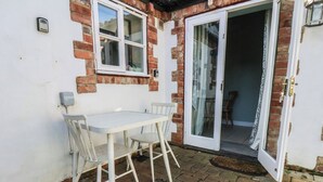 A patio with a table and chairs, a sliding glass door, and a brick wall. - Puffin's Nest (Bridlington)