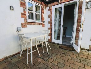 A patio with a table and chairs, a sliding glass door, and a brick wall. - Puffin's Nest (Bridlington)