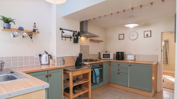 A compact kitchen with a sink, stove, microwave, and a small table with a kettle. - Puffin's Nest (Bridlington)