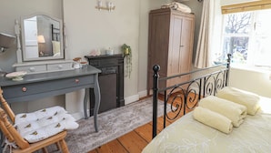 Une chambre à coucher comprenant un lit, une commode, un bureau, une chaise, un miroir, une fenêtre avec des rideaux et une vue sur l’extérieur.