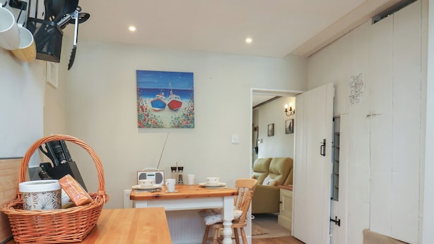 Une cuisine chaleureuse avec une table en bois, des chaises et une radio. Un tableau représentant des bateaux est accroché au mur.