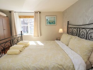 A bedroom with a bed, a window with curtains, a painting on the wall, and a wooden wardrobe. - Seashell Cottage (Bridlington)