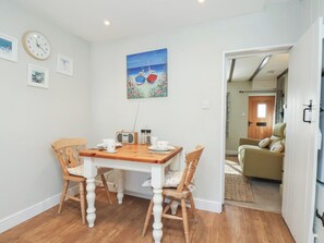 A dining area with a wooden table, chairs, a clock, and a painting. - Seashell Cottage (Bridlington)
