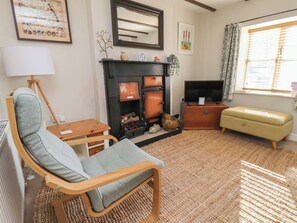 A living room with a fireplace, a television, a sofa, a wooden chair, and a window with curtains. - Seashell Cottage (Bridlington)