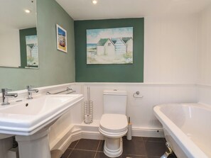 A bathroom with a sink, toilet, and bathtub, with green walls and two paintings. - Seashell Cottage (Bridlington)