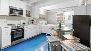 A modern kitchen with white cabinetry, stainless steel appliances, a blue floor, and a round glass table with benches. - Beachfront Studio w/ Pool, Steps to Sand, Sleeps 3 (Panama City Beach)