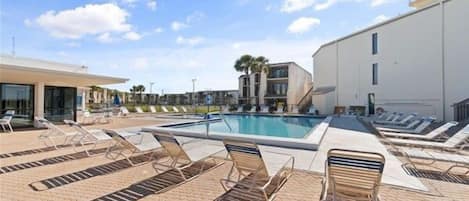 Un espace piscine avec des chaises longues et un bâtiment en arrière-plan.