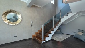 Een modern interieur met een trap, een ronde spiegel met een getande lijst, en een lichtgekleurde muur.