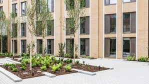 Een modern gebouw met veel ramen en een aangelegde binnentuin met bomen en planten.