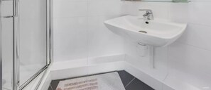 A bathroom with a glass shower enclosure, a white sink with a chrome faucet, and a small shelf above the sink. - Student only Modern Studio at White city (London)