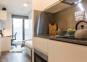 A modern kitchen with a built-in oven, a kettle, and a cutting board. - Student only Modern Studio at White city (London)