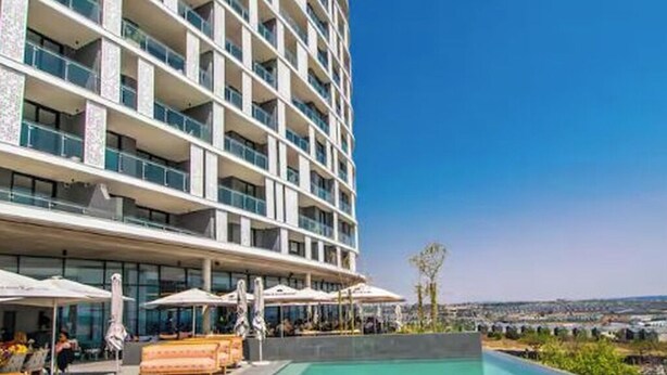 Ein modernes Hotel mit großem Pool, Sitzgelegenheiten im Freien und Blick auf die Stadt.