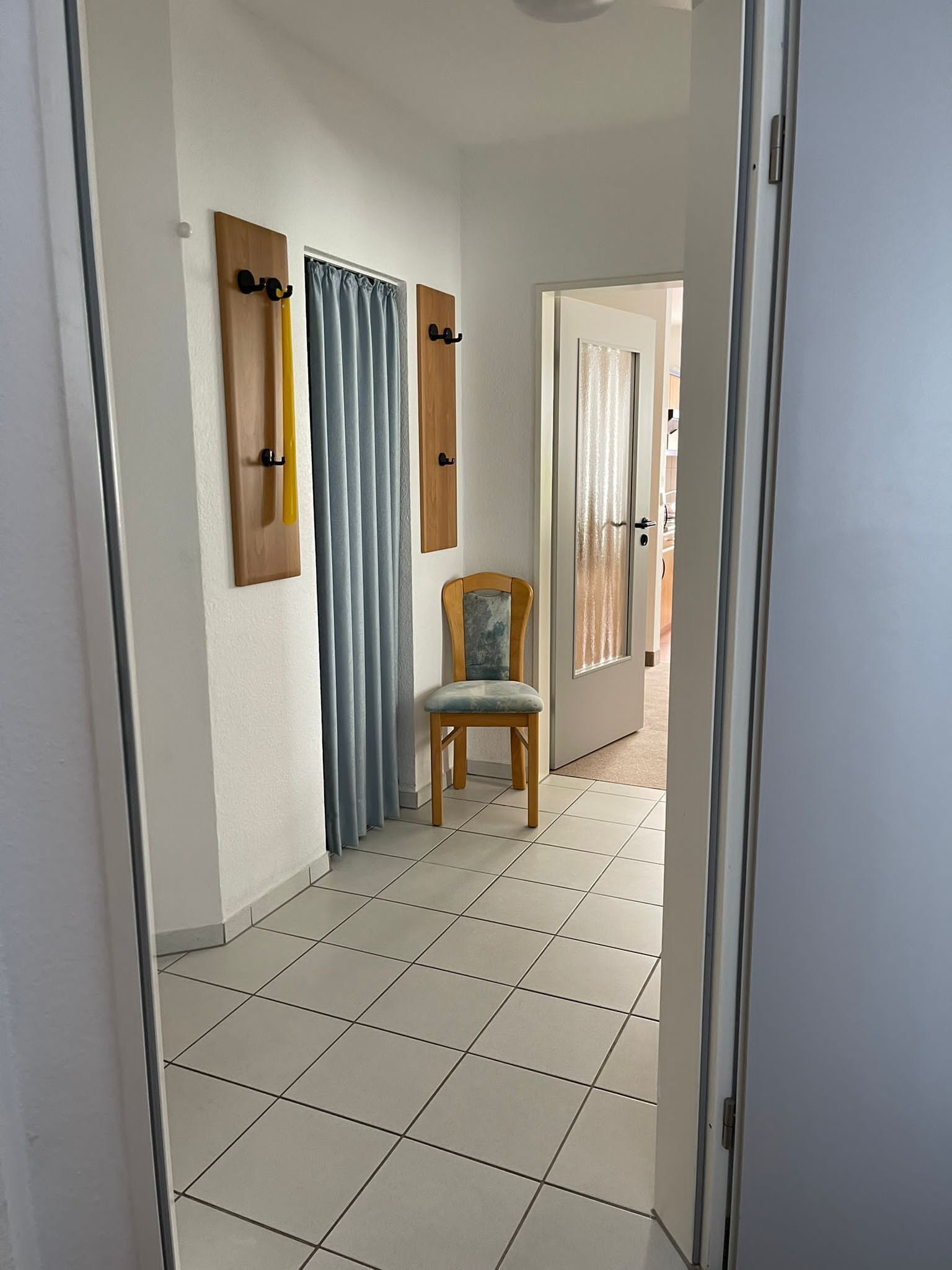 A hallway with a chair, a wooden coat rack, and a door leading to another room.