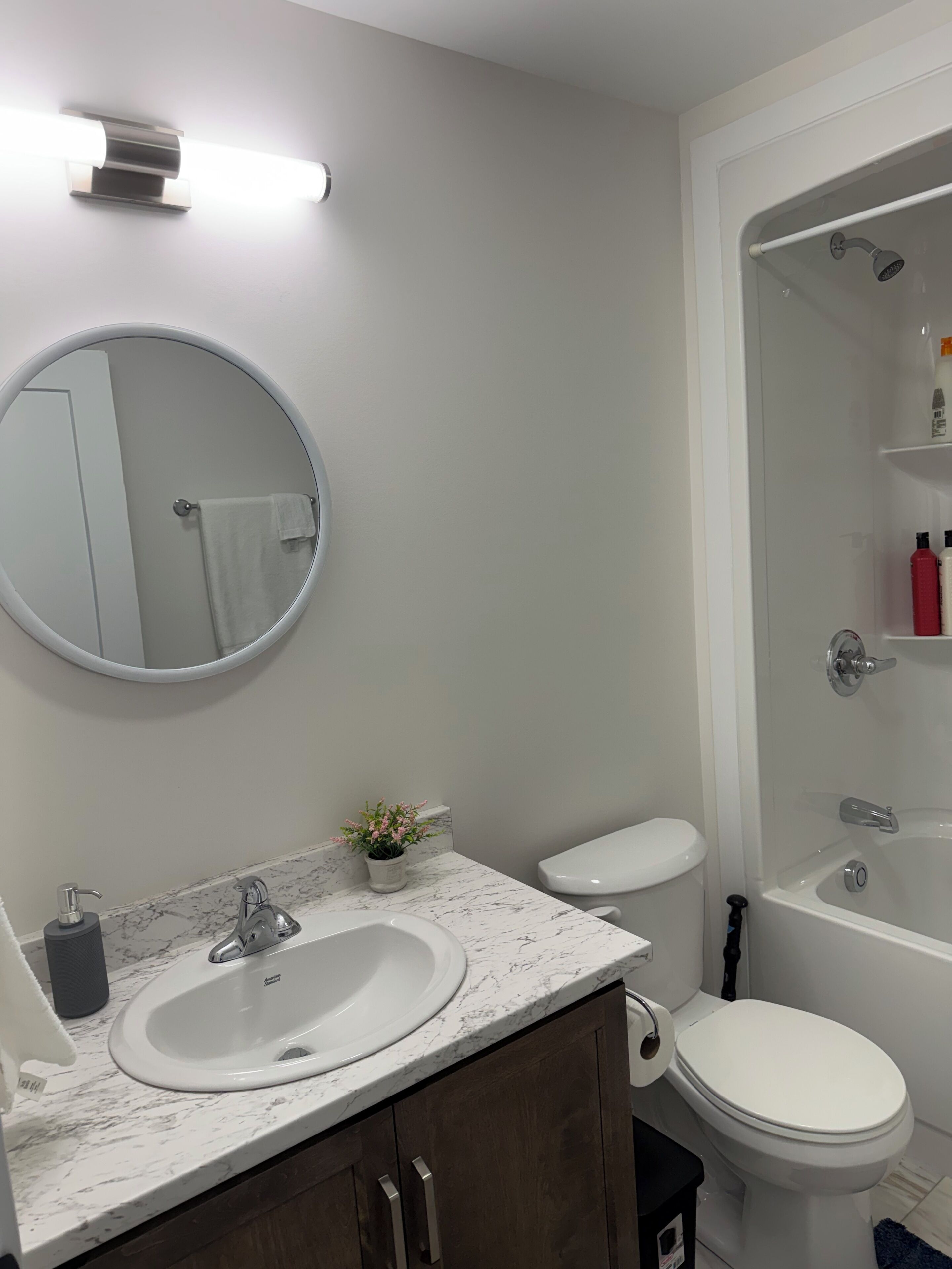 A modern bathroom with a round mirror, two sinks, a toilet, and a shower area.