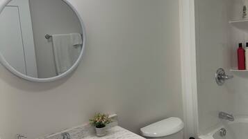 A modern bathroom with a round mirror, two sinks, a toilet, and a shower area.