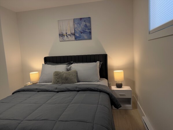 Un lit bien fait, avec une tête de lit noire, deux tables de chevet avec des lampes et un tableau accroché au mur.