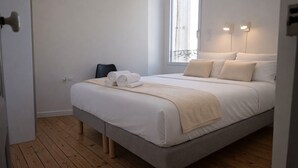Siististi pedattu sänky, jossa on vaaleanbeige peitto, kaksi tyynyä ja rullalle taitetut valkoiset pyyhkeet.