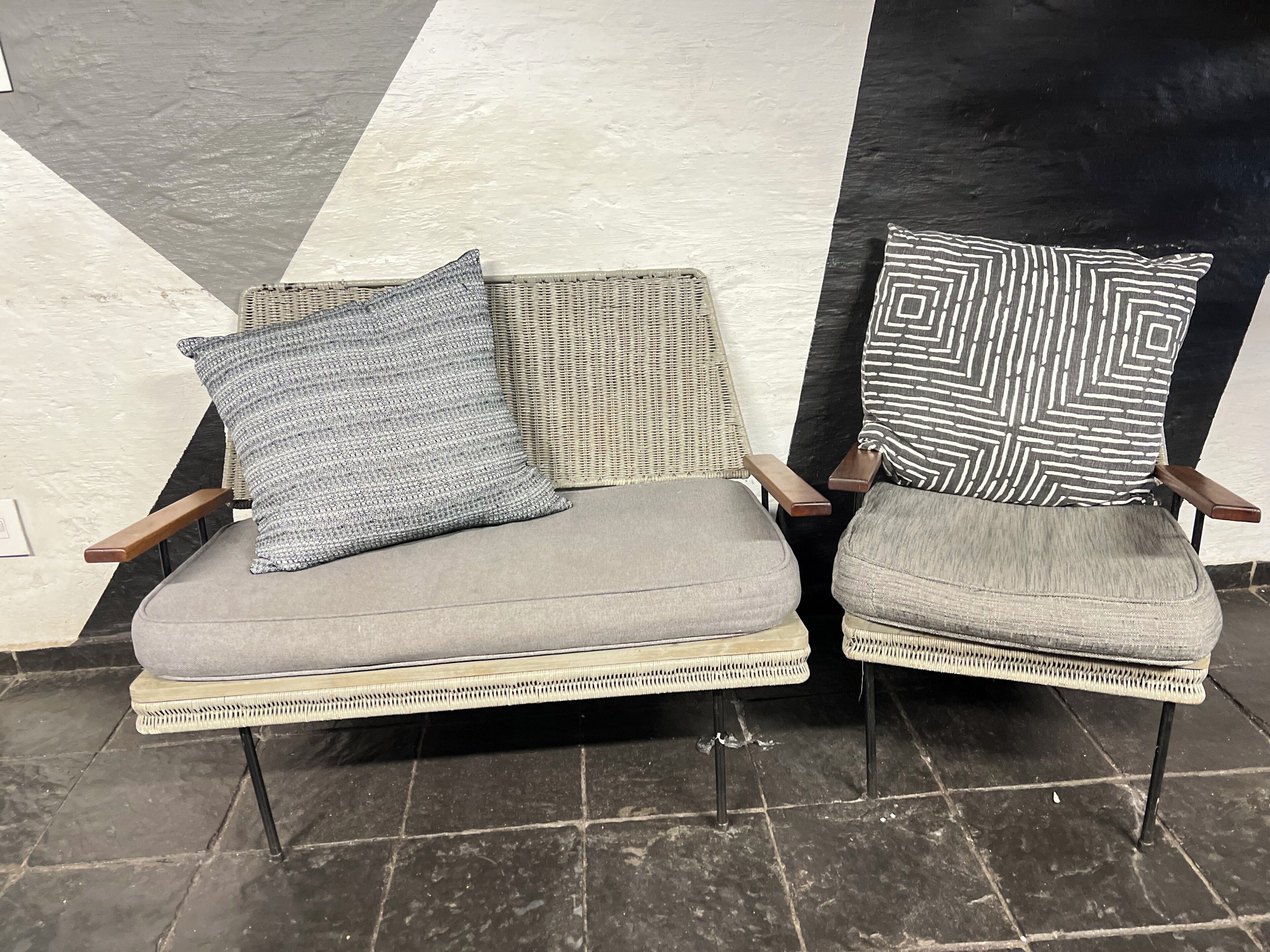 Zwei Korbstühle mit Kissen und gemusterten Sitzkissen auf einem Fliesenboden.