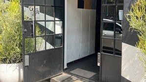 Een gebouw-ingang met een zwarte deur, een bord waarop 'MABO NENG' staat, en een bloempot met een plantje aan de linkerkant.