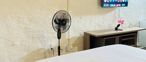 A bedroom with a bed, a wall-mounted TV, a fan, and a clock.