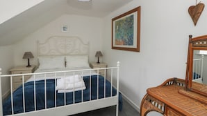 A bedroom with a white metal bed frame, a blue mattress, two bedside lamps, a wall-mounted painting, and a wooden chair. - Holly Cottage (Inveraray)