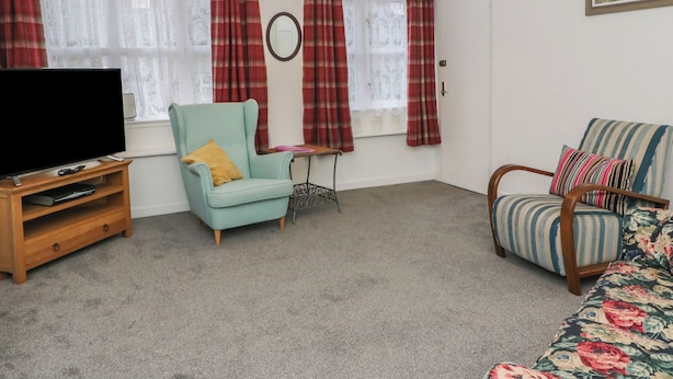 A living room with a television, two armchairs, a small table, and a painting on the wall. - Holly Cottage (Inveraray)