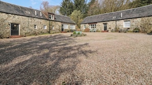 A stone building with a gravel driveway and a small garden area. - Holly Cottage (Inveraray)