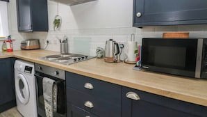 A modern kitchen with a washing machine, microwave, toaster, kettle, and cabinets. - Holly Cottage (Inveraray)