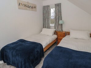 Een slaapkamer met twee bedden, een nachtkastje, een lamp en een raam met gordijnen.