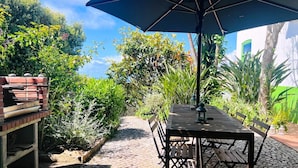 En terrasse med et bord, stole, en murstensgrill og en stor parasol.