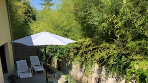 Eine Terrasse mit Tisch, Stühlen und Sonnenschirm, mit Blick auf einen Fluss.