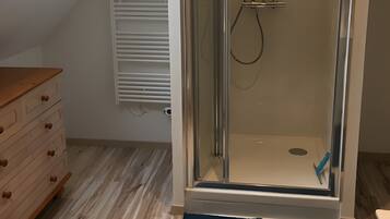 A shower with a glass door, a wooden dresser, and a skylight.
