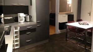 Uma cozinha moderna com forno embutido, cafeteira e torradeira. Há uma área de refeições com mesa e cadeiras.