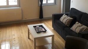 Sala de estar com um sofá preto, uma mesa de centro branca e uma janela com cortinas.