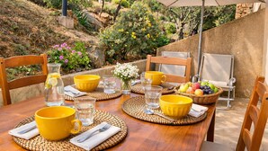 Un espace de restauration en plein air avec une table dressée pour deux personnes, agrémentée de bols jaunes, de verres à eau et d’un panier de fruits.