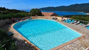 Une piscine à l’eau d’un bleu cristallin, entourée de chaises longues et d’une terrasse en pierre.
