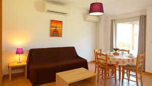 Ein Wohnzimmer mit Sofa, einem kleinen Tisch, einem Esstisch mit Stühlen, einer Klimaanlage und einem Bild an der Wand.