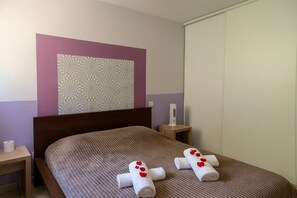 A hotel room with a bed, a wall with a textured pattern, a bedside table with a lamp, and a window with blinds. - new 2026 F2 pour 4 à 5 personnes tout équipé dans résidence piscine et mer (SERRA DI FERRO)