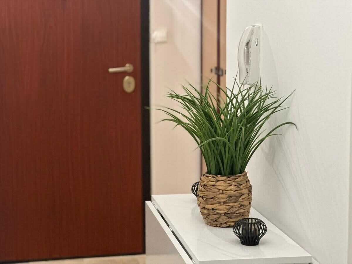 A wooden door, a white wall, a woven plant pot, and a small black object on a white shelf.