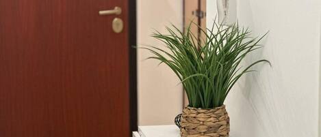 A wooden door, a white wall, a woven plant pot, and a small black object on a white shelf.