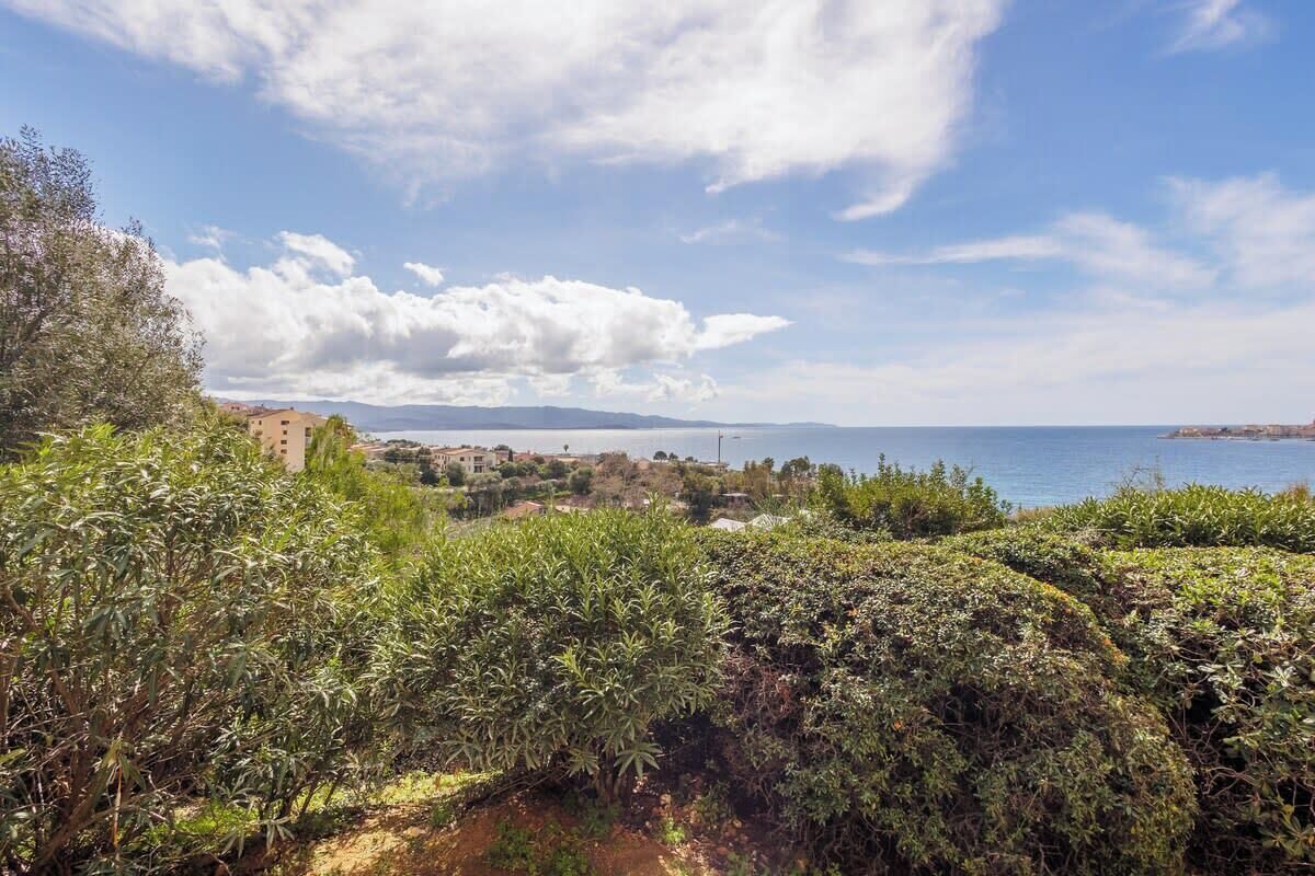 Eine Küstenlandschaft mit dichter Vegetation, einem entfernten Gebäude und blauem Himmel.