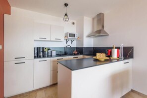 Eine moderne Küche mit weißen Schränken, einer schwarzen Arbeitsplatte, einer Mikrowelle, einer Kaffeemaschine und einer Edelstahl-Dunstabzugshaube.