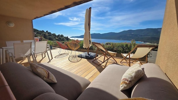 Ein Balkon mit Holzboden, gepolsterten Sitzgelegenheiten und Blick auf einen See und Berge.