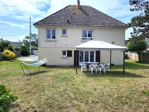 Une maison à deux étages, avec un toit en tuiles, une terrasse couverte avec des chaises et un hamac.
