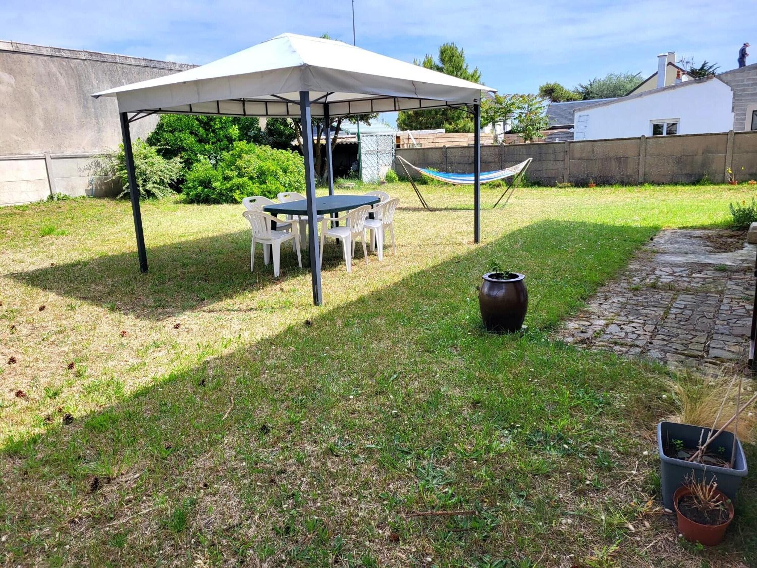 A covered outdoor seating area with a table and chairs, a hammock, and a potted plant.